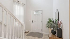 Un escalier avec des balustrades blanches, une porte blanche dotée d’un panneau en verre dépoli et un miroir posé sur une console en bois, agrémentée de deux vases.