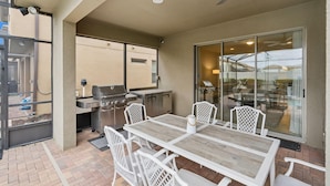 Une terrasse extérieure avec un barbecue, des chaises blanches et une table.