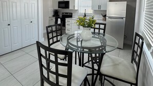 Cozinha moderna com armários brancos, mesa de jantar de vidro e uma placa com a palavra 'Fresh' acima do micro-ondas.