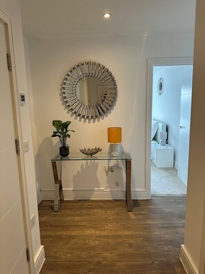 A hallway with a glass console table, a decorative mirror, a potted plant, and a lamp. - Spacious 2-Bed, 2-Bath Apartment | Contractor, Insurance & Relocation Friendly (Southampton)