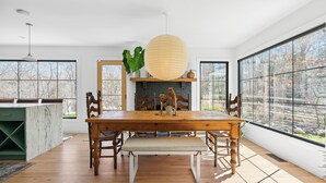 Un comedor con una mesa de madera, sillas, un banco, una lámpara colgante y una chimenea.