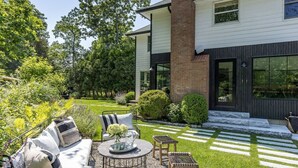 Una casa moderna con un jardín cuidado, mobiliario exterior y una vista despejada del jardín delantero.
