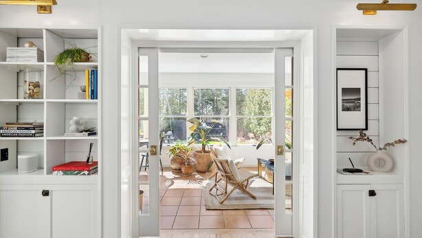 Una habitación con un ventanal amplio, una estantería, una silla y una puerta que da al exterior.