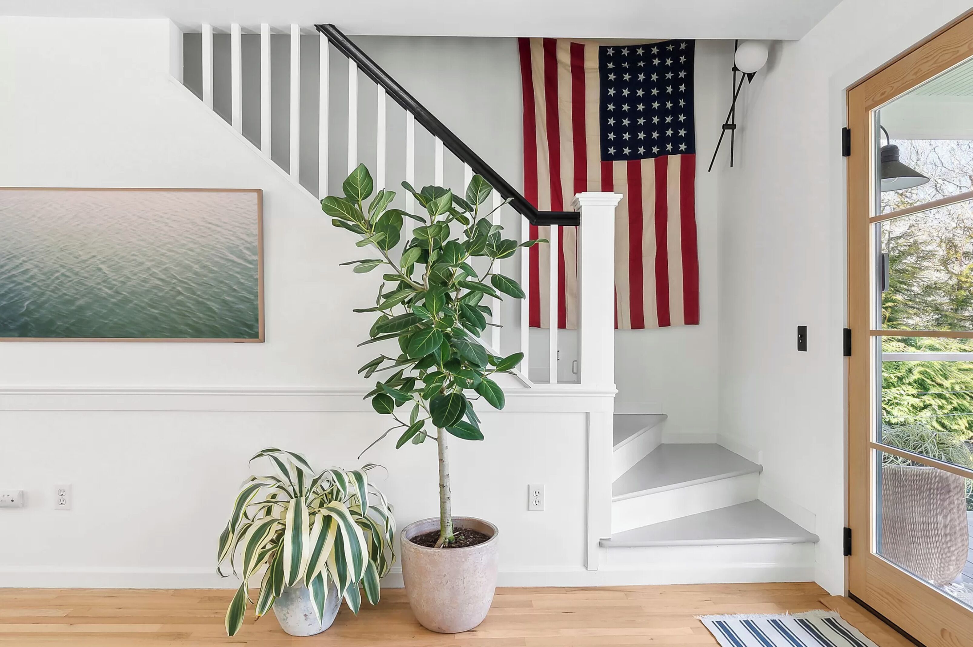 A staircase with white railings, an American flag, a potted plant, and a framed artwork.