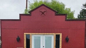 Un bâtiment rouge avec une porte blanche, deux fenêtres et deux lampes fixées au mur.