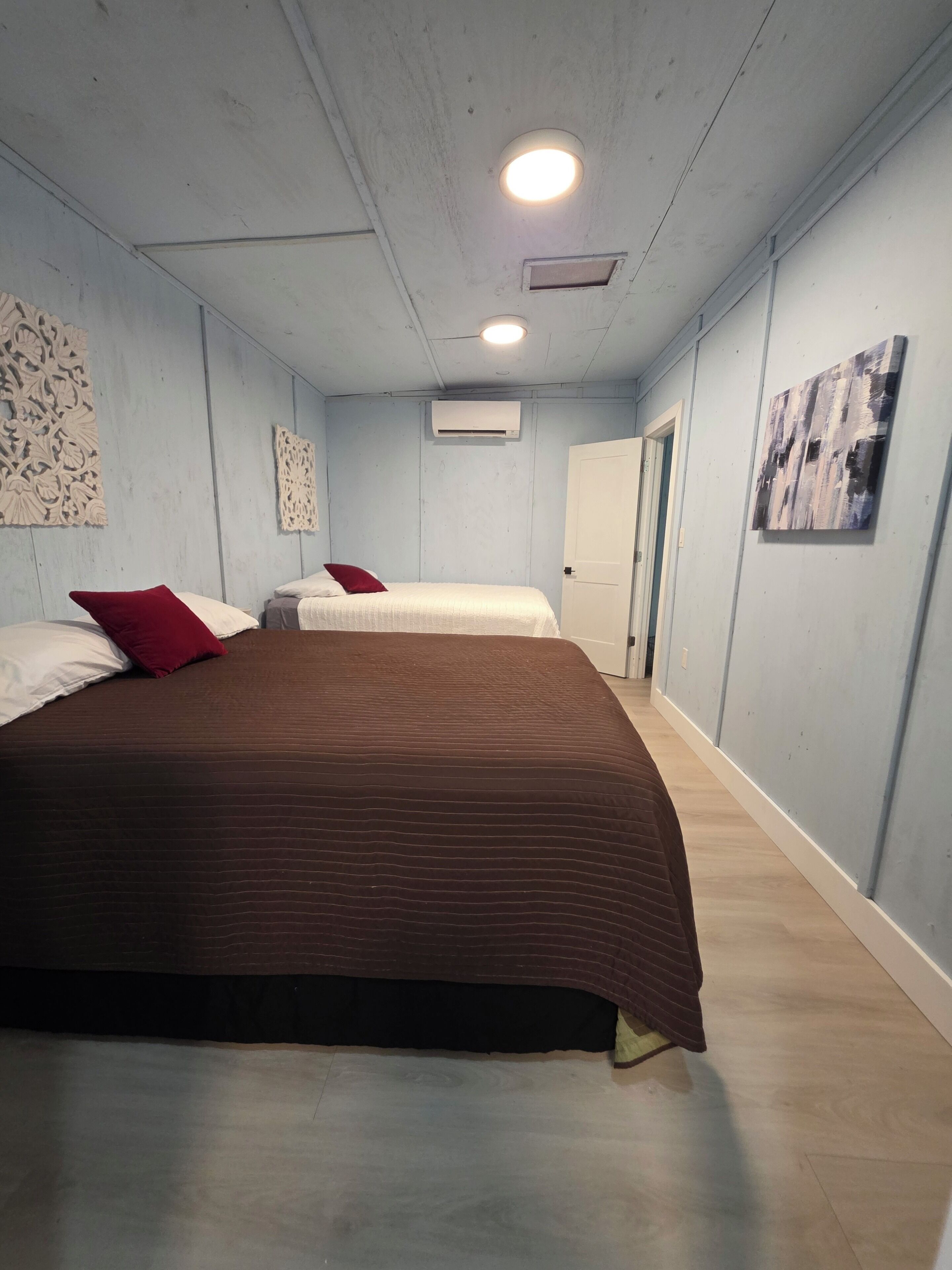 A room with two beds, a ceiling light, an air conditioning unit, and a door.