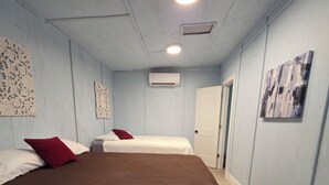Une chambre avec deux lits, un luminaire au plafond, un appareil de climatisation et une porte.