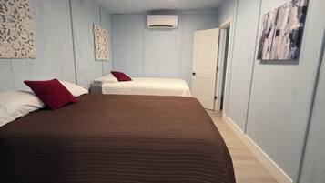 A room with two beds, a ceiling light, an air conditioning unit, and a door.