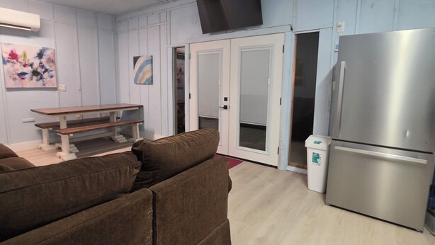 Un salon comprenant un canapé, un banc, un ventilateur de plafond, un téléviseur à écran plat, un réfrigérateur et une poubelle.