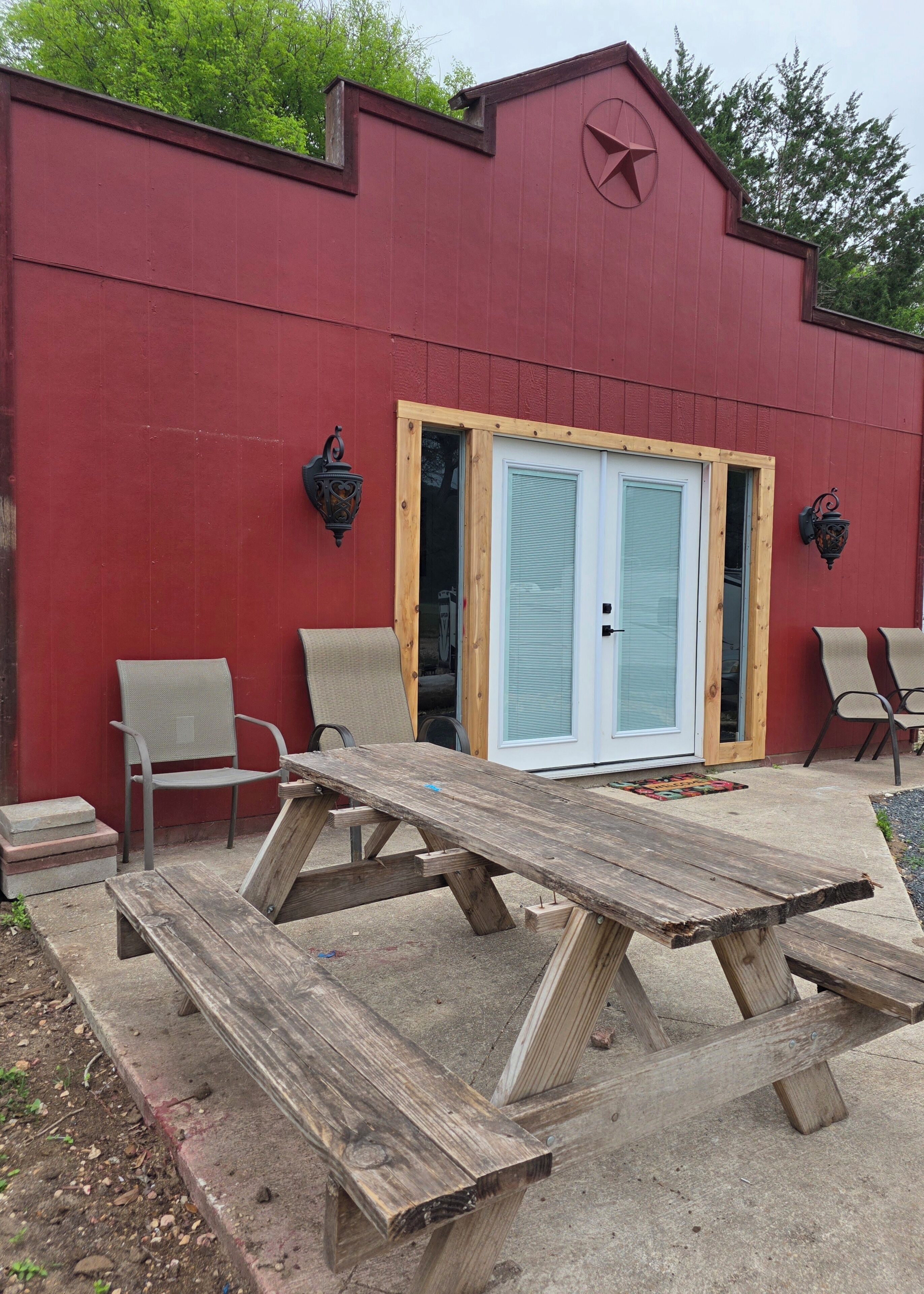 A red building with a white door, two chairs, a wooden table, and a small step leading to the door.