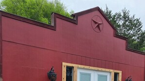 Un bâtiment rouge avec une porte blanche, deux chaises, une table en bois et une petite marche menant à la porte.