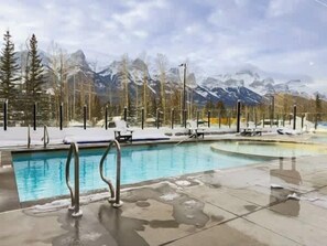 A pool with a view of snow-capped mountains and trees. - Spring Oasis: Brand New, Hot Tub/Pool, AC, Parking (Canmore)