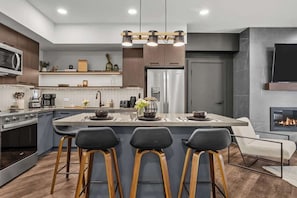 A modern kitchen with a central island, bar stools, a built-in oven, and a stainless steel refrigerator. - Spring Oasis: Brand New, Hot Tub/Pool, AC, Parking (Canmore)