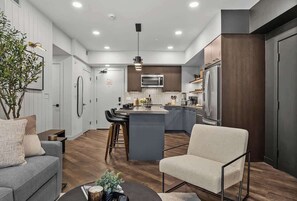 A modern kitchen with a central island, bar stools, and a dining area with a sofa and coffee table. - Spring Oasis: Brand New, Hot Tub/Pool, AC, Parking (Canmore)