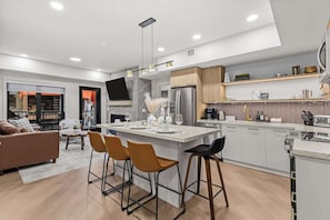 A modern kitchen with a central island, bar stools, and a dining area with a sofa and chairs. - Ascent Luxe Retreat | Brand-New 2BR (Canmore)