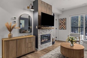 Ein modernes Wohnzimmer mit Kamin, großem Flachbildfernseher, einer Holzkonsole und einem großen Fenster.