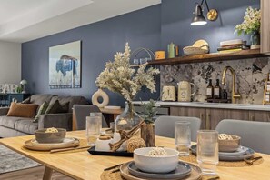 Ein modernes Wohnzimmer mit Essbereich, einer Küche mit Marmorarbeitsplatten und einer blauen Akzentwand.