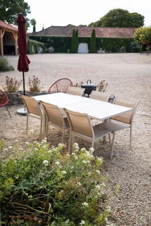An outdoor dining area with a table and chairs, surrounded by gravel, with a building and greenery in the background. - LOGIS DU PARADIS (Criteuil-la-Magdeleine)