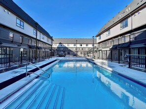 A swimming pool with steps leading into it, surrounded by buildings with balconies and railings. - Skyline Peaks Mountain Retreat - Studio (Canmore)