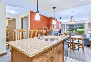 Cocina con encimeras de granito, pileta doble, muebles de madera e iluminación colgante.