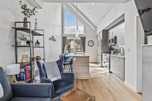A modern living room with a sofa, a coffee table, a bookshelf, and a dining area with chairs and a table. - Skyline Peaks Panorama Retreat (Canmore)