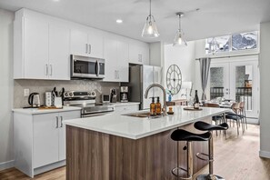 Een moderne keuken met witte kasten, roestvrijstalen apparatuur, een houten eiland en een zithoek met barstoelen.