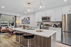 Een moderne keuken met een centraal eiland, roestvrijstalen apparatuur en hangende lampen.
