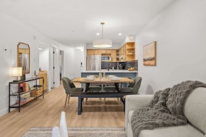 A modern kitchen with wooden cabinets, a dining table with chairs, and a cozy living area with a sofa and a blanket. - Magpie Lookout - Newly Renovated Mountain Escape (Canmore)