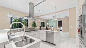 A modern kitchen with a central island, stainless steel appliances, and a large window providing a view of greenery. - Luxury Villa w/ Heated Pool / Jacuzzi / 6BR /Games/ Miami (Miami)