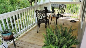 Een overdekt terras buiten, met een tafel en stoelen, omgeven door potplanten en een witte balustrade.