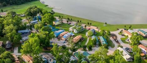 An aerial view of a lakeside campground with RVs and cabins, surrounded by trees and a lake.