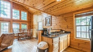 A wooden cabin interior with a kitchen, dining area, and a trash bin. - Water's Edge RV Resort (Willis)