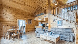 A wooden cabin interior with a dining area, sofa, and staircase. - Water's Edge RV Resort (Willis)