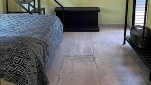 Quarto com beliche, escada, um pequeno banco preto e uma cesta.