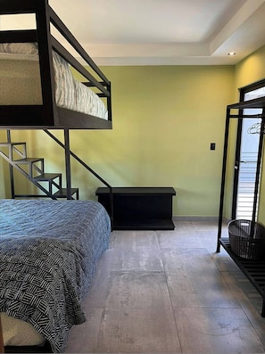Une chambre avec un lit superposé, un escalier, un petit banc noir et un panier.