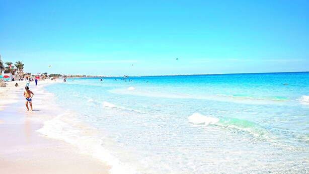 A beach with clear water, a sandy shore, and a few people.