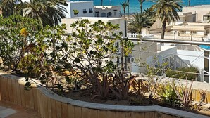 A terrace with tiled flooring, a low retaining wall, and a view of the sea and buildings.