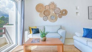 A living room with a white sofa, a wooden coffee table with a plant, and a wall decorated with woven circular art pieces. - Playa Condo, Private Rooftop Terrace & Pool (Playa del Carmen)
