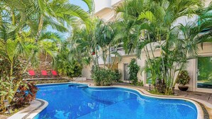 A swimming pool surrounded by lush greenery and red lounge chairs. - Playa Condo, Private Rooftop Terrace & Pool (Playa del Carmen)