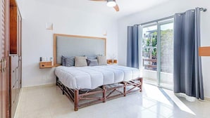 A bedroom with a bed, a ceiling fan, a window with curtains, and a view of the outside. - Playa Condo, Private Rooftop Terrace & Pool (Playa del Carmen)