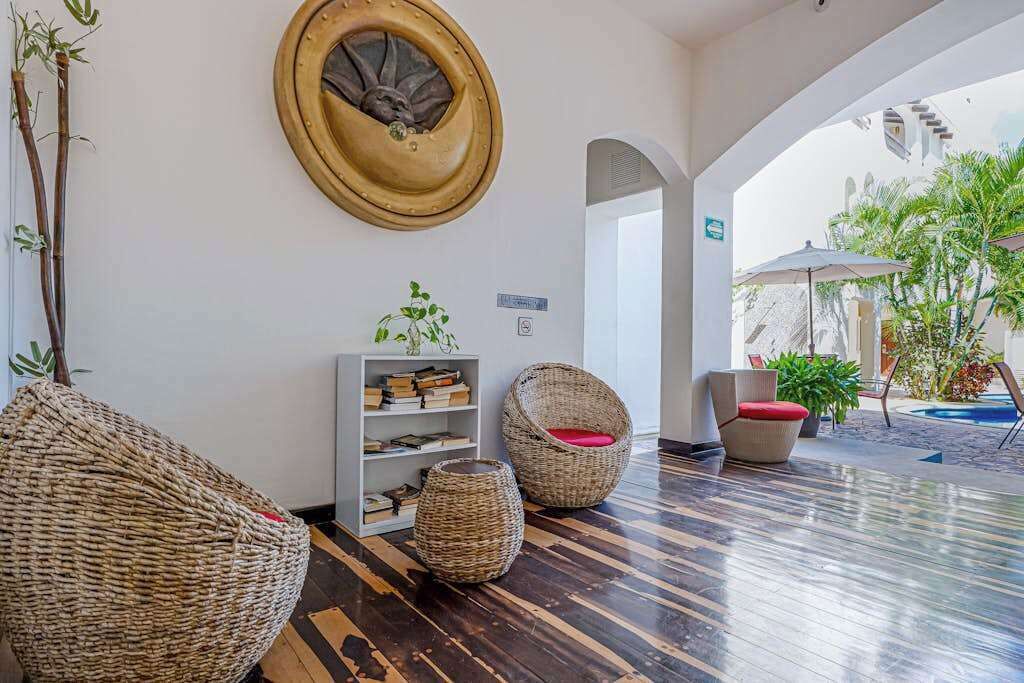 A lobby with wicker furniture, a round wall decoration, a bookshelf, and an outdoor area with plants.