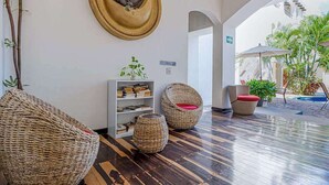A lobby with wicker furniture, a round wall decoration, a bookshelf, and an outdoor area with plants. - Playa Condo, Private Rooftop Terrace & Pool (Playa del Carmen)