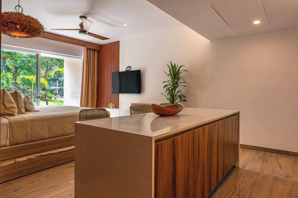 Una sala de estar moderna con un sofá, un comedor con una isla de madera, un televisor de pantalla plana montado en la pared y un ventanal con vistas a zonas verdes.