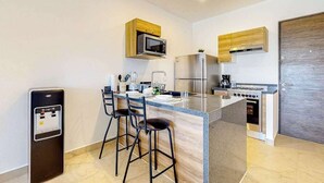 Una cocina moderna con una isla central, taburetes de bar, microondas, refrigerador, estufa y cafetera.