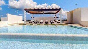 Piscina con sillones de descanso y una pérgola bajo un cielo despejado.