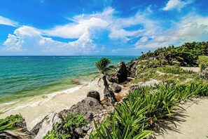 A coastal landscape with a beach, rocky outcrops, and lush greenery. - 2BR condo near Akumal beach, rooftop pool (Akumal)