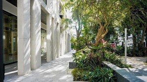 Un edificio moderno con facciata in vetro, un vialetto lastricato e un'area verde con alberi e piante.
