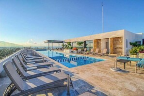 Ett poolområde på taket med solstolar, en pool och en byggnad med stora fönster.