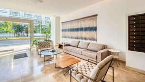 A spacious living room with a sofa, armchairs, a coffee table, and a wall-mounted TV. - Luxury Condo: Rooftop Pool, Jacuzzi & Game Room (Playa del Carmen)