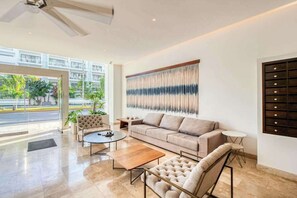 A spacious living room with a sofa, armchairs, a coffee table, and a wall-mounted TV. - Luxury Condo: Rooftop Pool, Jacuzzi & Game Room (Playa del Carmen)